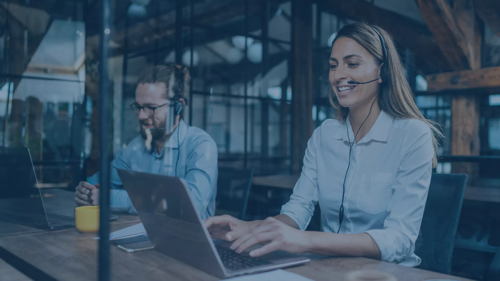 Zwei IT-Support-Mitarbeitende arbeiten mit Headsets und Laptops in einem modernen Büro. Sie bieten proaktiven, skalierbaren und sicheren IT-Support, um Ausfälle zu verhindern, Geschäftsprozesse zu optimieren und die Zukunftsfähigkeit von Unternehmen zu sichern.