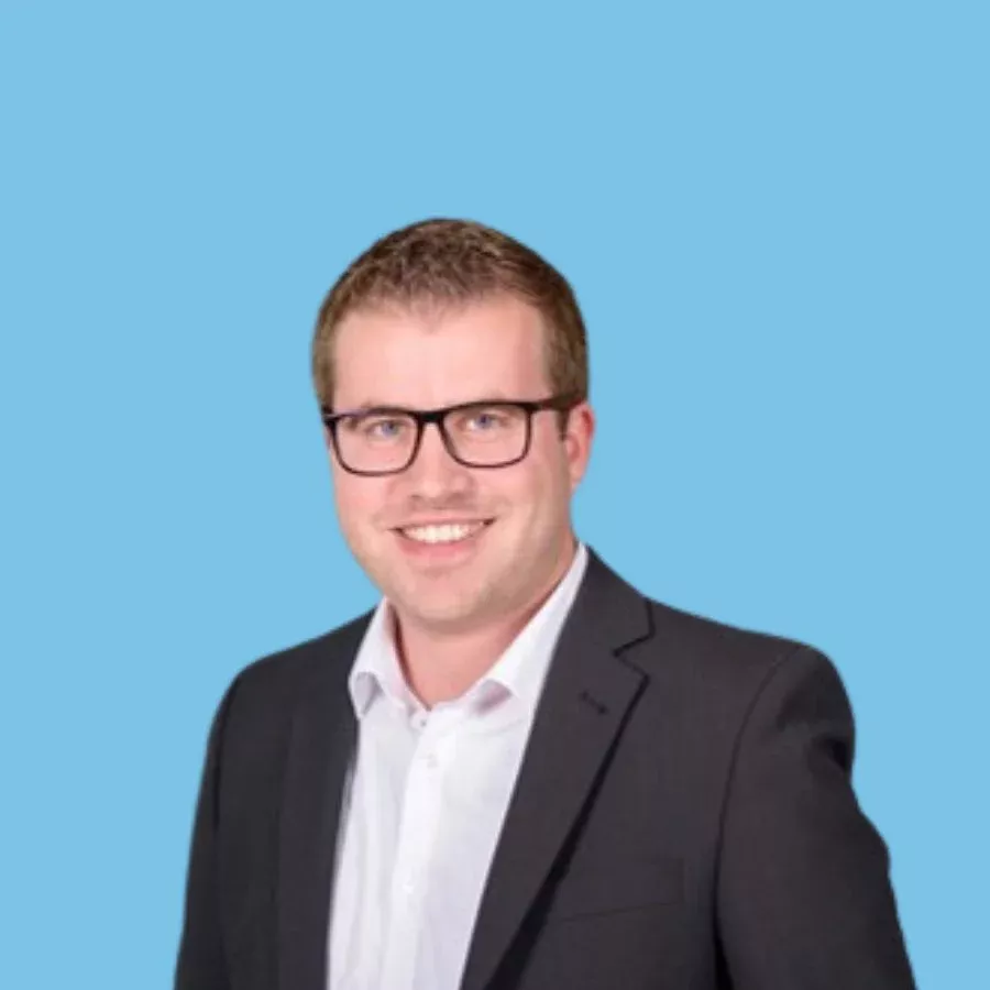 Porträtfoto eines lächelnden Mannes (Daniel Mörgenthaler) im Business-Outfit vor blauem Hintergrund.