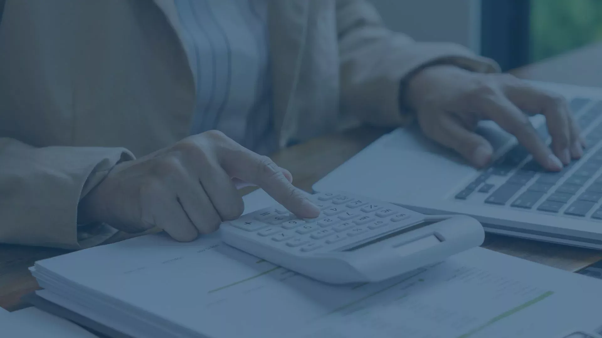 Person arbeitet mit Taschenrechner und Laptop an steuerrelevanten Unterlagen.